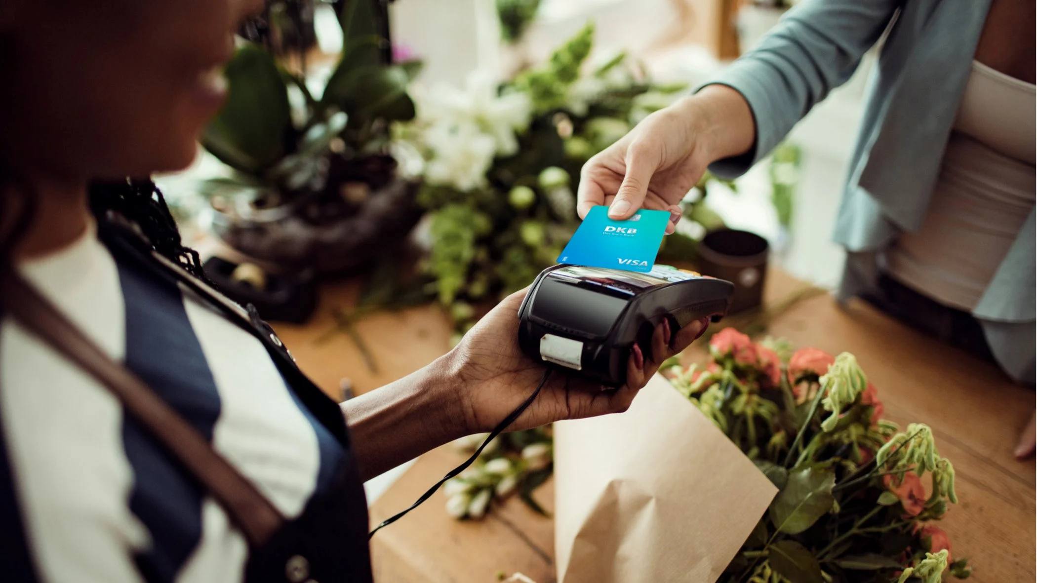 Eine Frau bezahlt einen Blumenstrauß mit einer Visa Debitkarte der DKB.