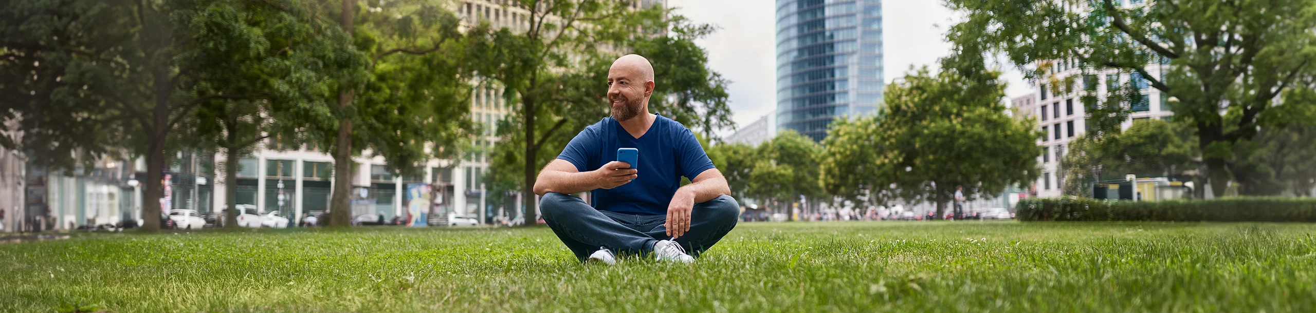 Mann mit Handy sitzt auf Wiese