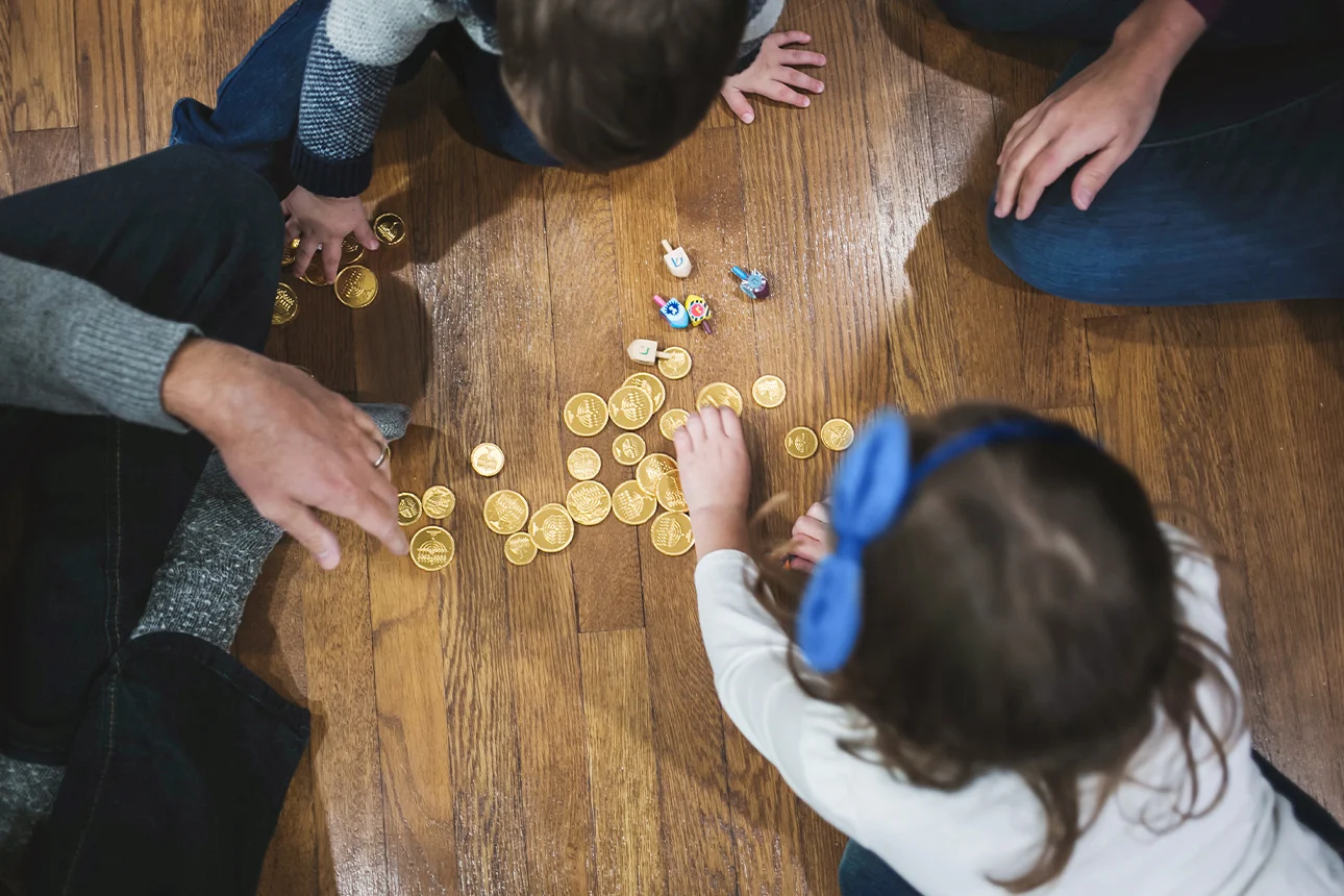 Vier Personen, darunter zwei Kinder, sitzen in einem Kreis auf dem Boden und schauen sich Geldmünzen an.
