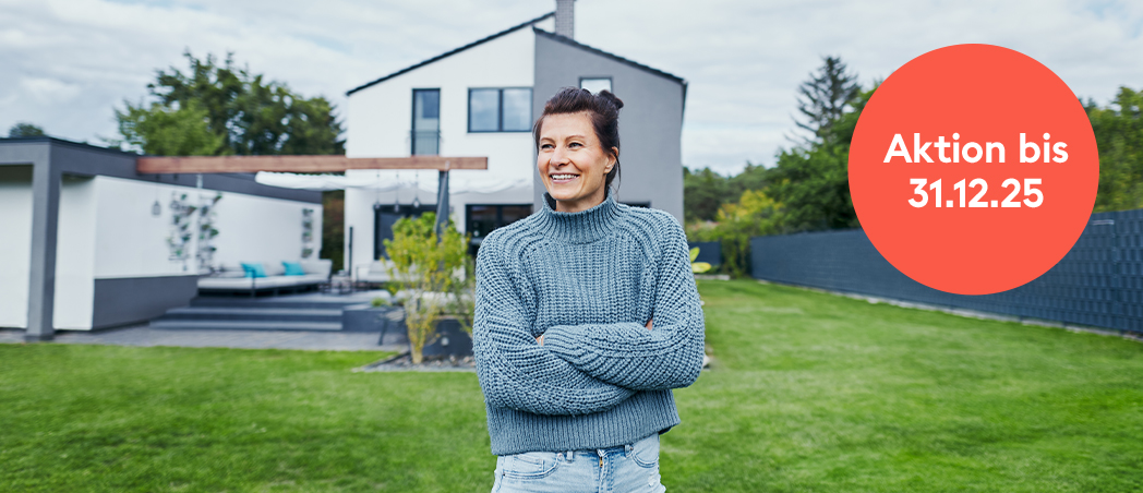 Frau steht im Garten vor Einfamilienhaus und freut sich