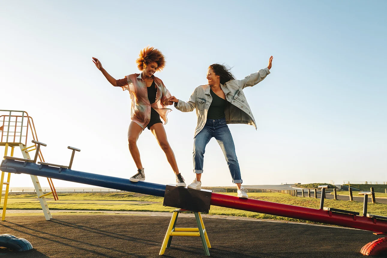 Zwei Frauen balancieren auf einer Wippe auf einem Spielplatz.
