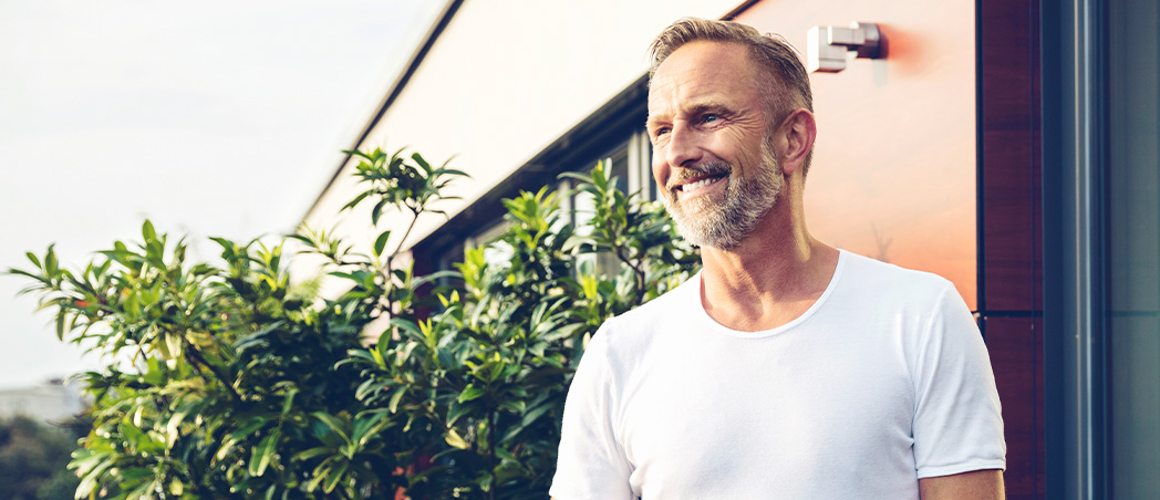 Ein lachender Mann im T-Shirt steht auf einem Balkon