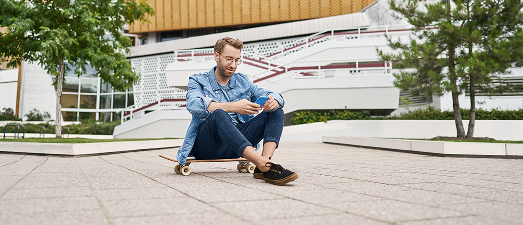 Mann mit Handy sitzt auf Skateboard