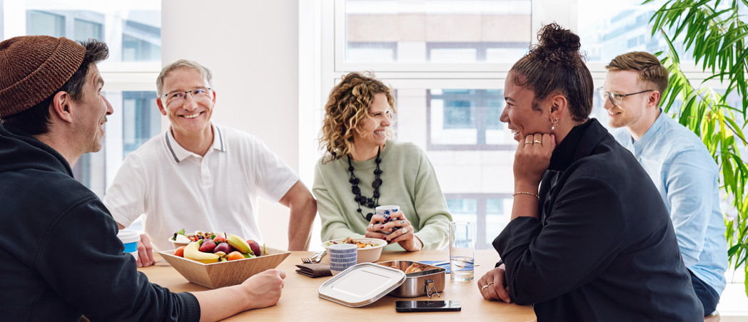 4 Personen sitzen beim Mittagessen an einem Küchentisch und lachen