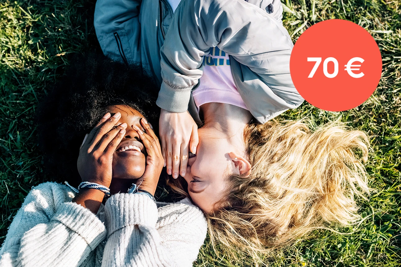Zwei Frauen liegen auf einer Wiese und flüstern sich etwas ins Ohr