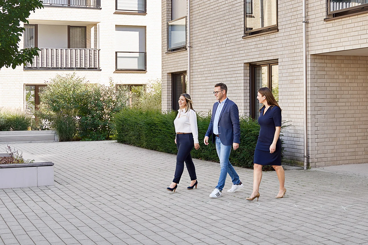 3 Personen überqueren Vorplatz eines verwalteten Gebäudes