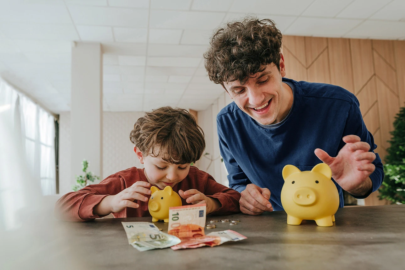 Vater und Sohn werfen gut gelaunt Geld in zwei Sparschweine