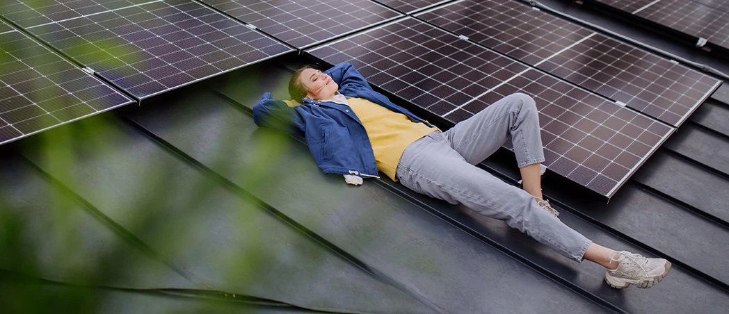 Frau liegt entspannt auf Hausdach neben Solarpanelen