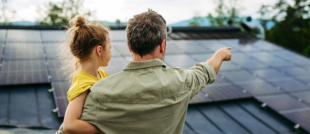 Vater und Tochter betrachten Solarmodule auf dem Hausdach