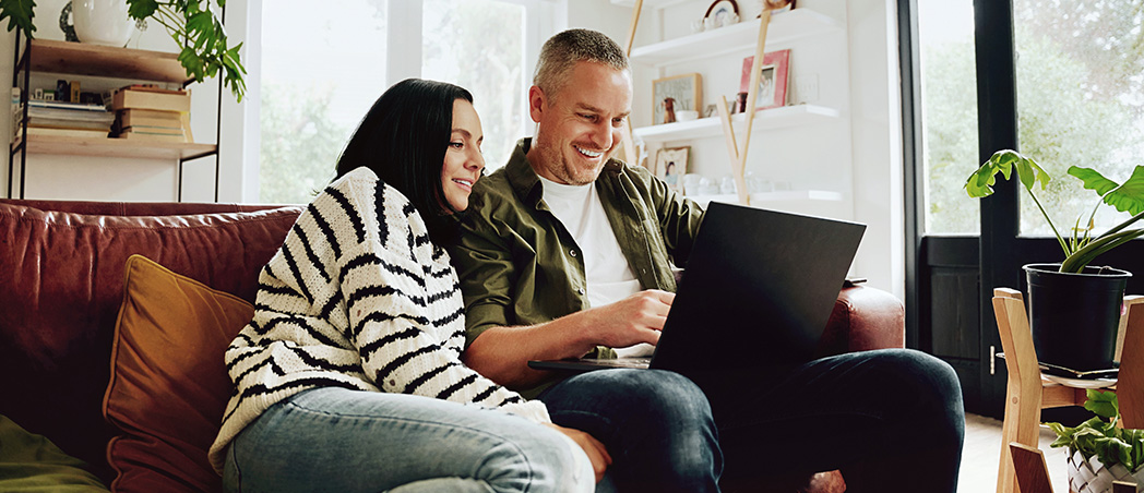 Ein Pärchen sitzt auf einer Couch, der Mann hat einen Laptop auf dem Schoß