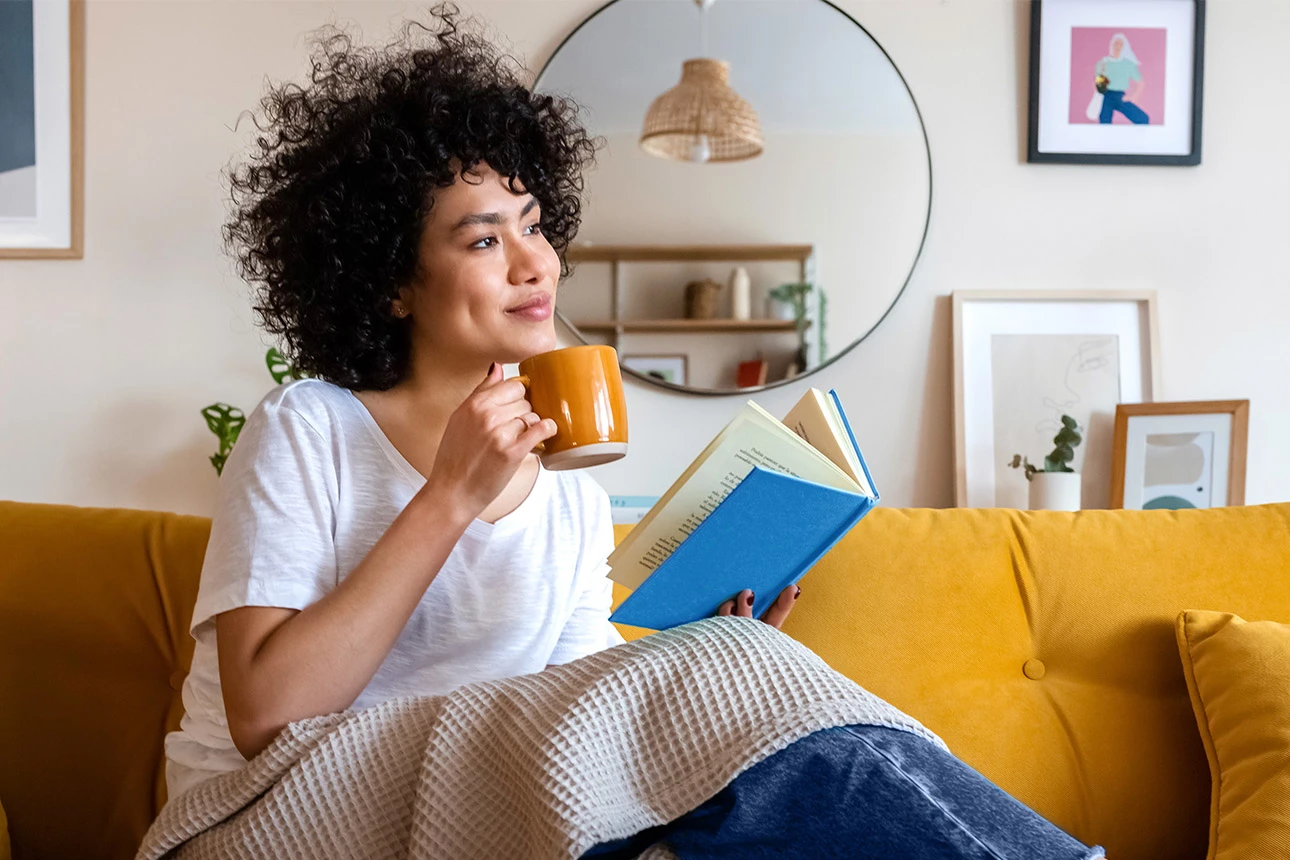 Frau sitzt mit Buch und Getränk auf der Couch