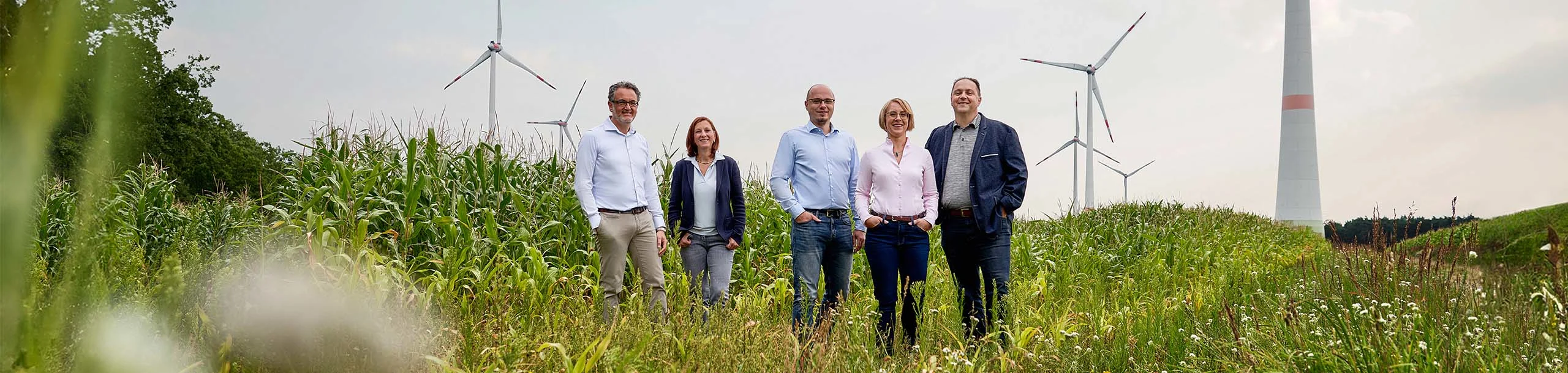 Eine Gruppe steht auf einem Feld mit Windrädern im Hintergrund