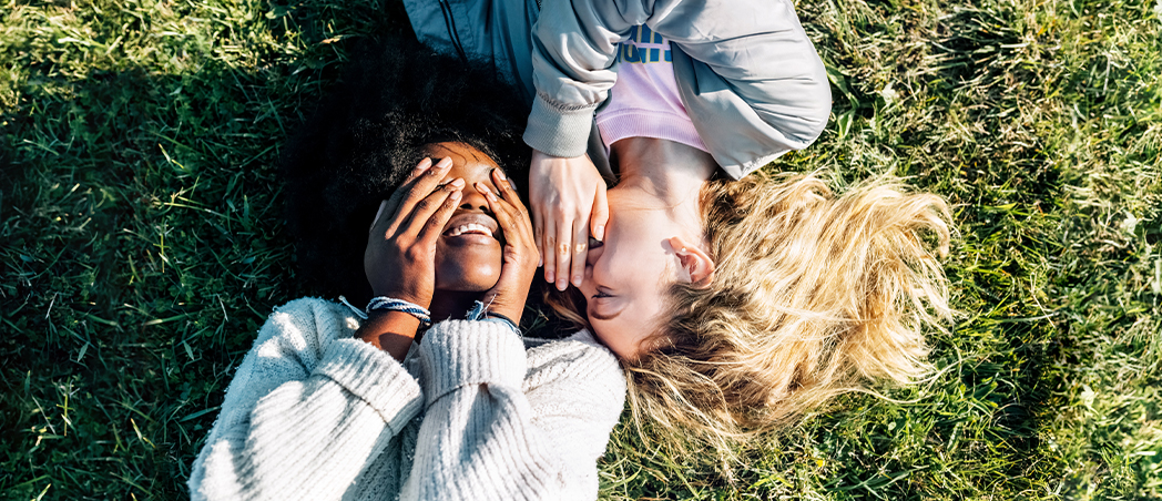 Zwei Frauen liegen auf einer Wiese und flüstern sich etwas ins Ohr