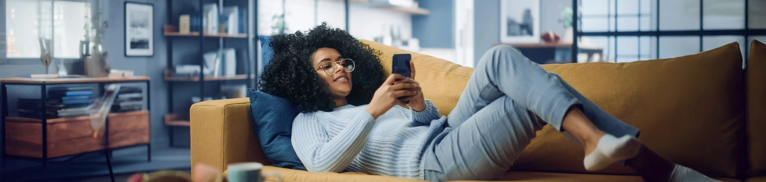 Junge Frau liegend auf Couch mit Handy in der Hand