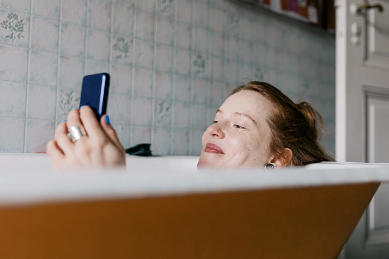 Eine Frau liegt in der Badewanne und schaut auf ihr Handy