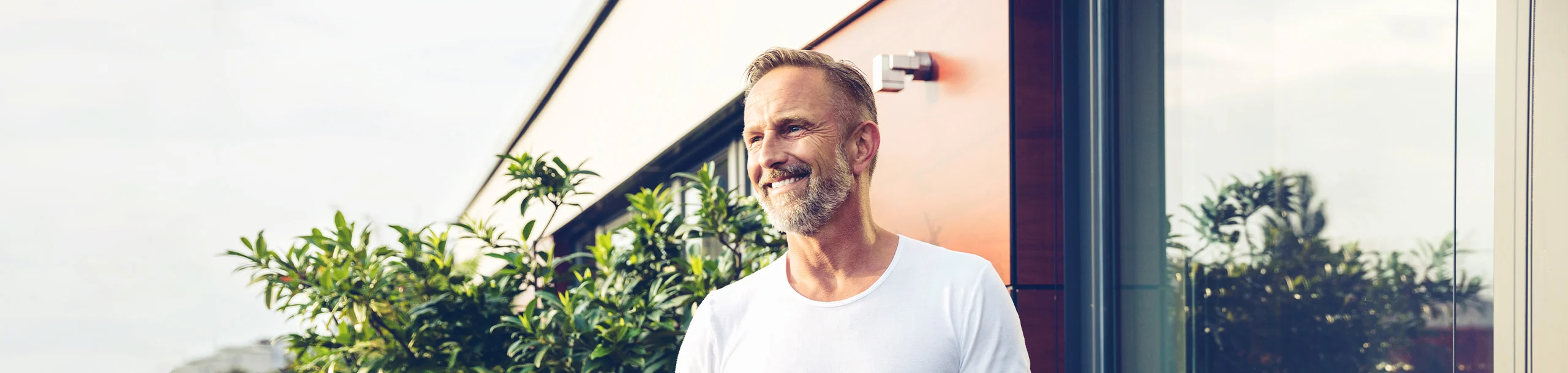 Ein lachender Mann im T-Shirt steht auf einem Balkon