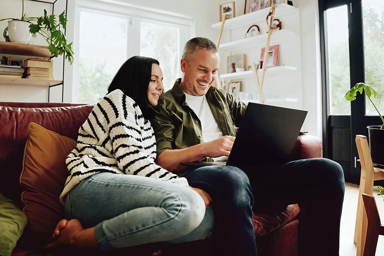 Ein Pärchen sitzt auf einer Couch, der Mann hat einen Laptop auf dem Schoß