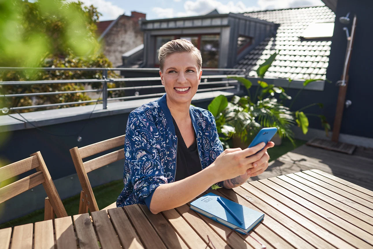 Frau mit bunter Jacke am Tisch mit Handy