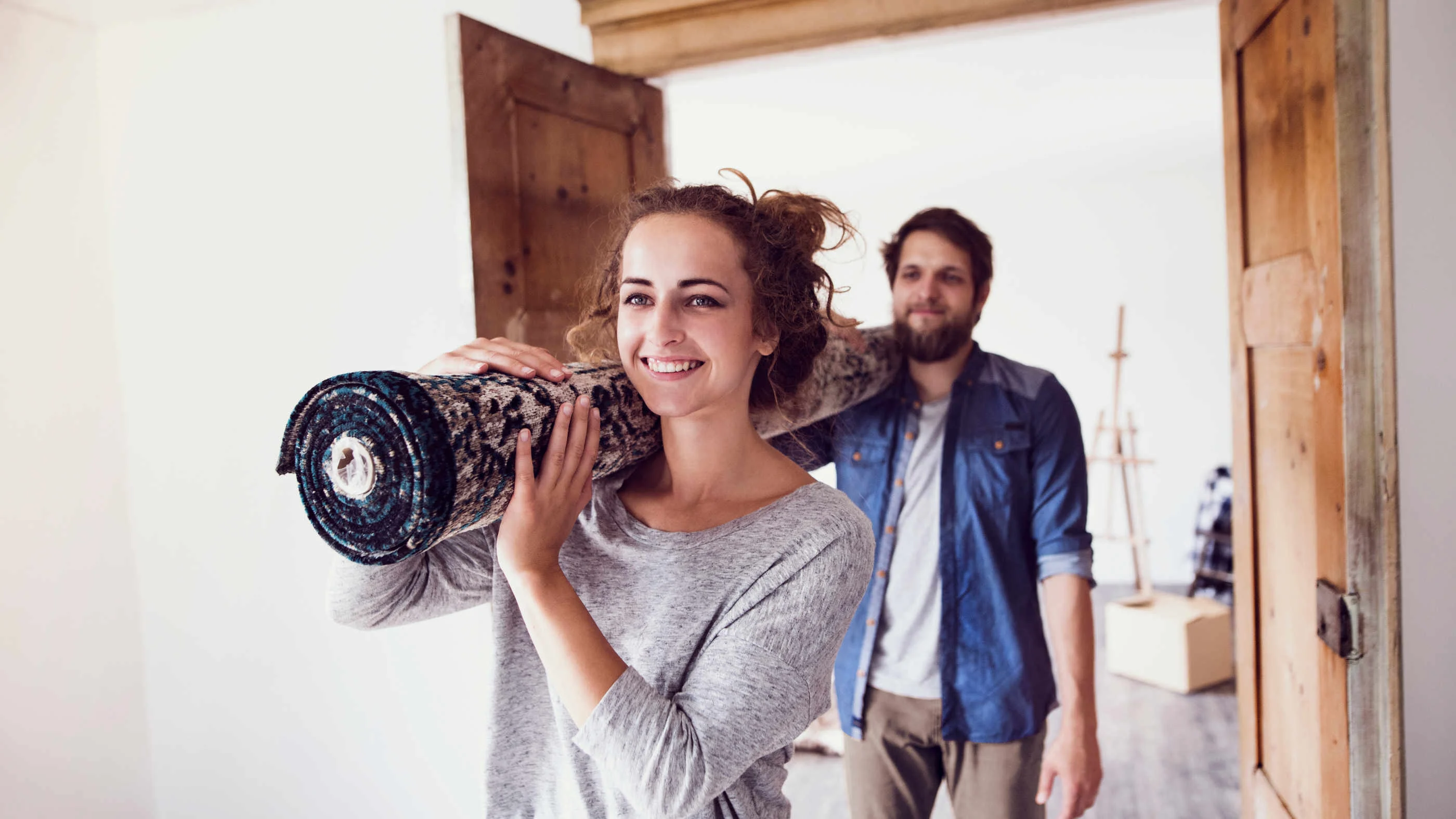 Ein Pärchen aus Mann und Frau trägt einen Teppich in die neue gemeinsame Wohnung.