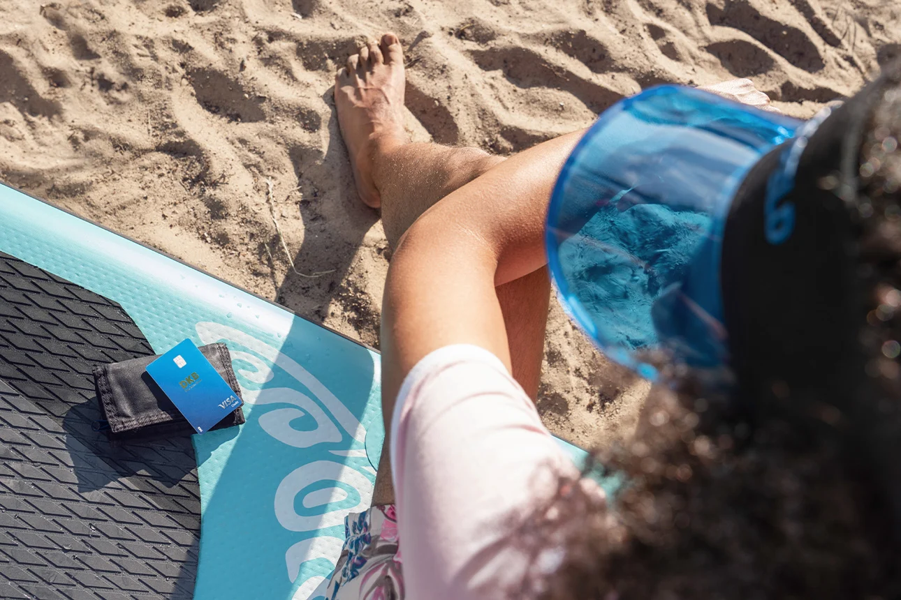 Person sitzt am Strand neben Geldbörse mit Visa Kreditkarte