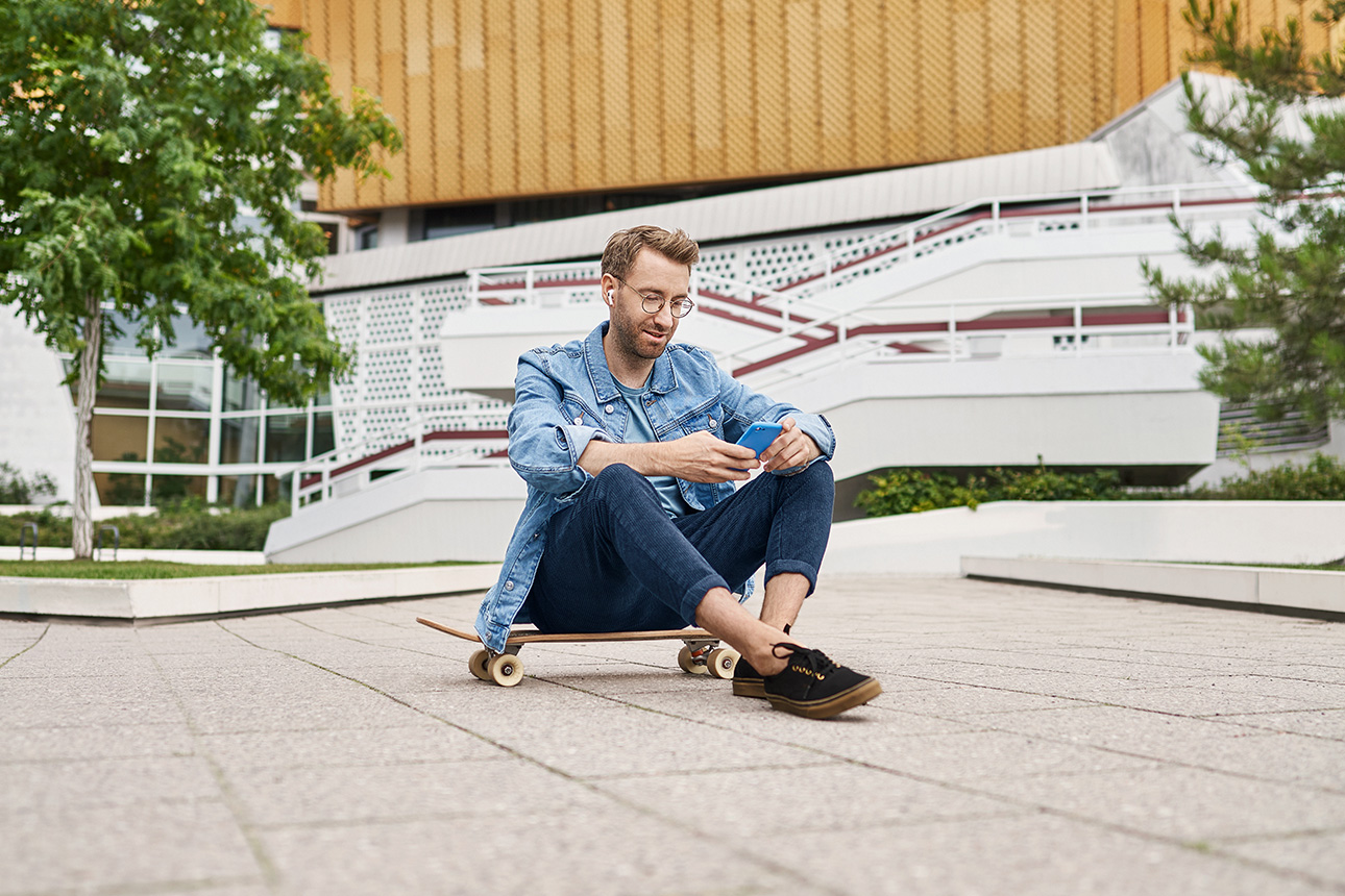 Mann mit Handy sitzt auf Skateboard