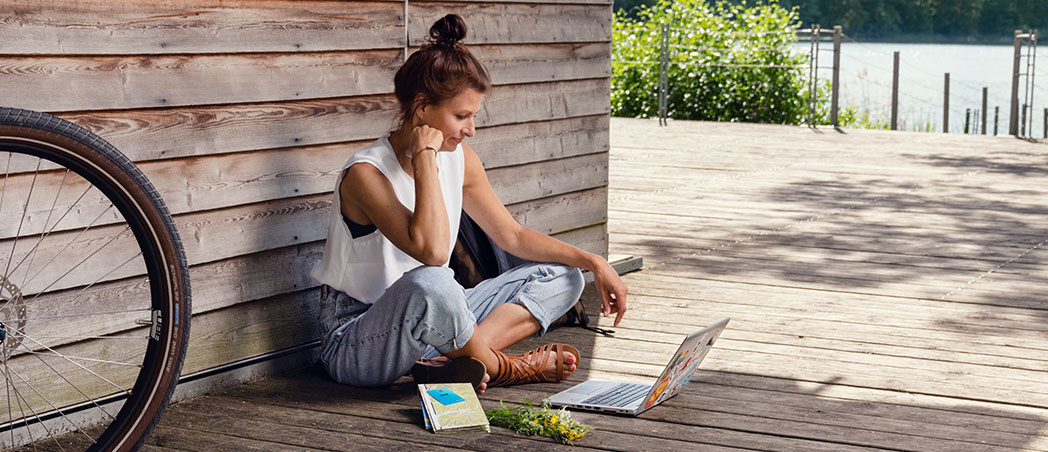 Frau sitzt am See mit Laptop und E-Bike