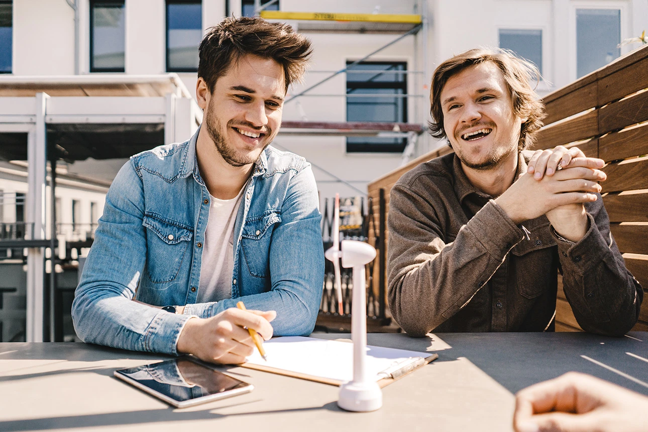 Zwei Männer sitzen an einem Tisch und lachen entspannt bei einem Gespräch