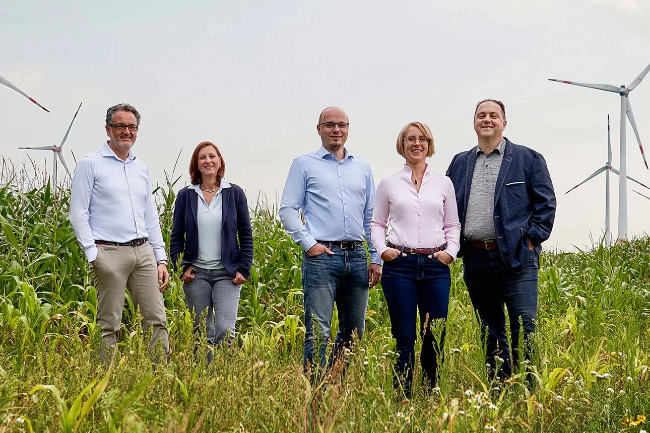 Eine Gruppe steht auf einem Feld mit Windrädern im Hintergrund