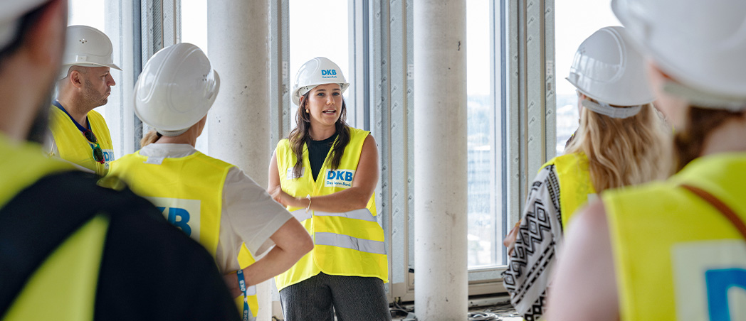 Gruppe von Menschen steht mit Helmen und gelben Sicherheitswesten auf einer Baustelle