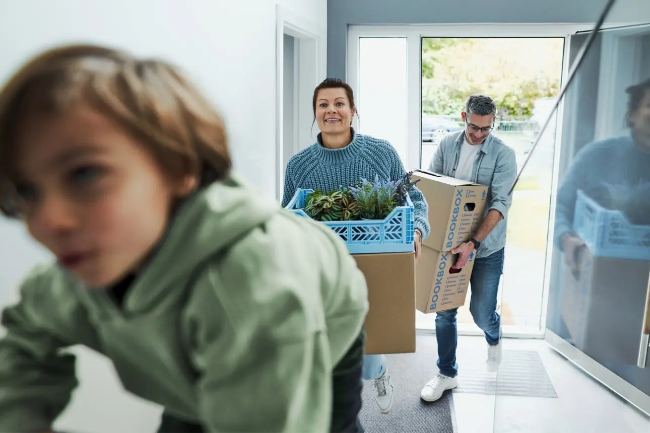 Familie mit Kind trägt Umzugskisten in ein neues Zuhause.