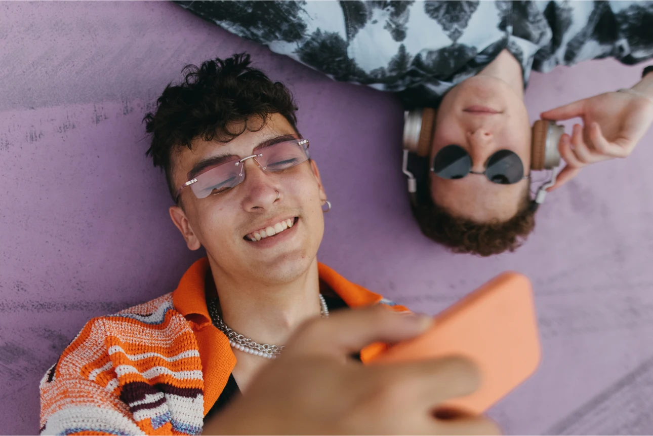 Zwei junge Menschen hören Musik mit Kopfhörern und schauen aufs Smartphone