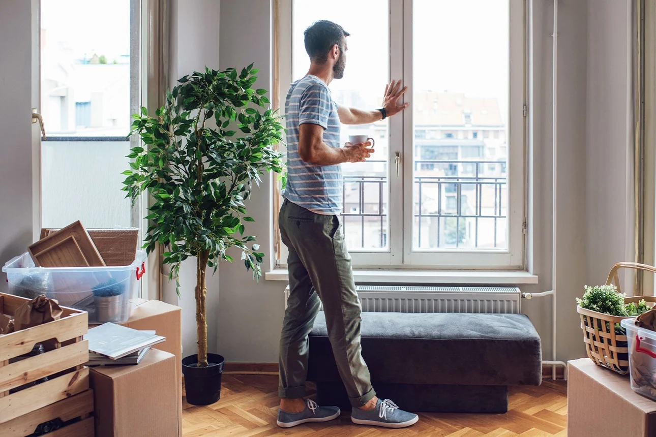 Ein Mann mit Kaffeetasse steht am Fenster einer neu bezogenen Wohnung