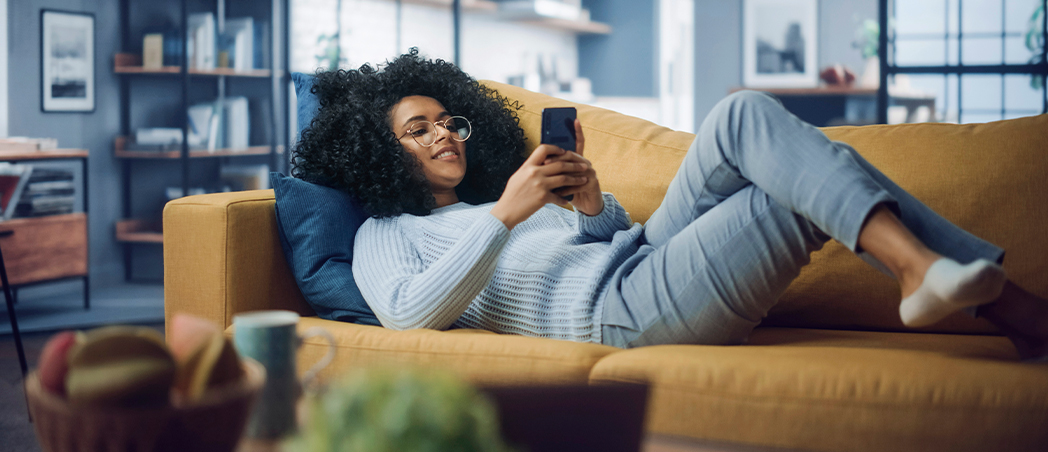 Junge Frau liegend auf Couch mit Handy in der Hand