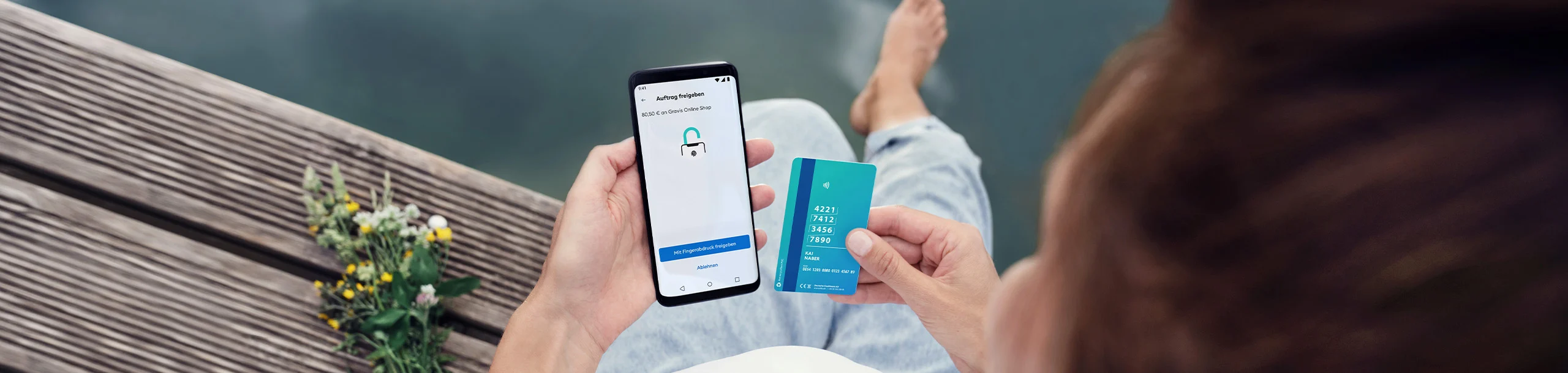 Person hält Visa Debitkarte, gibt Auftrag in DKB App frei