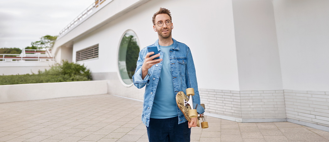 Ein Mann mit Smartphone und Skateboard in der Hand