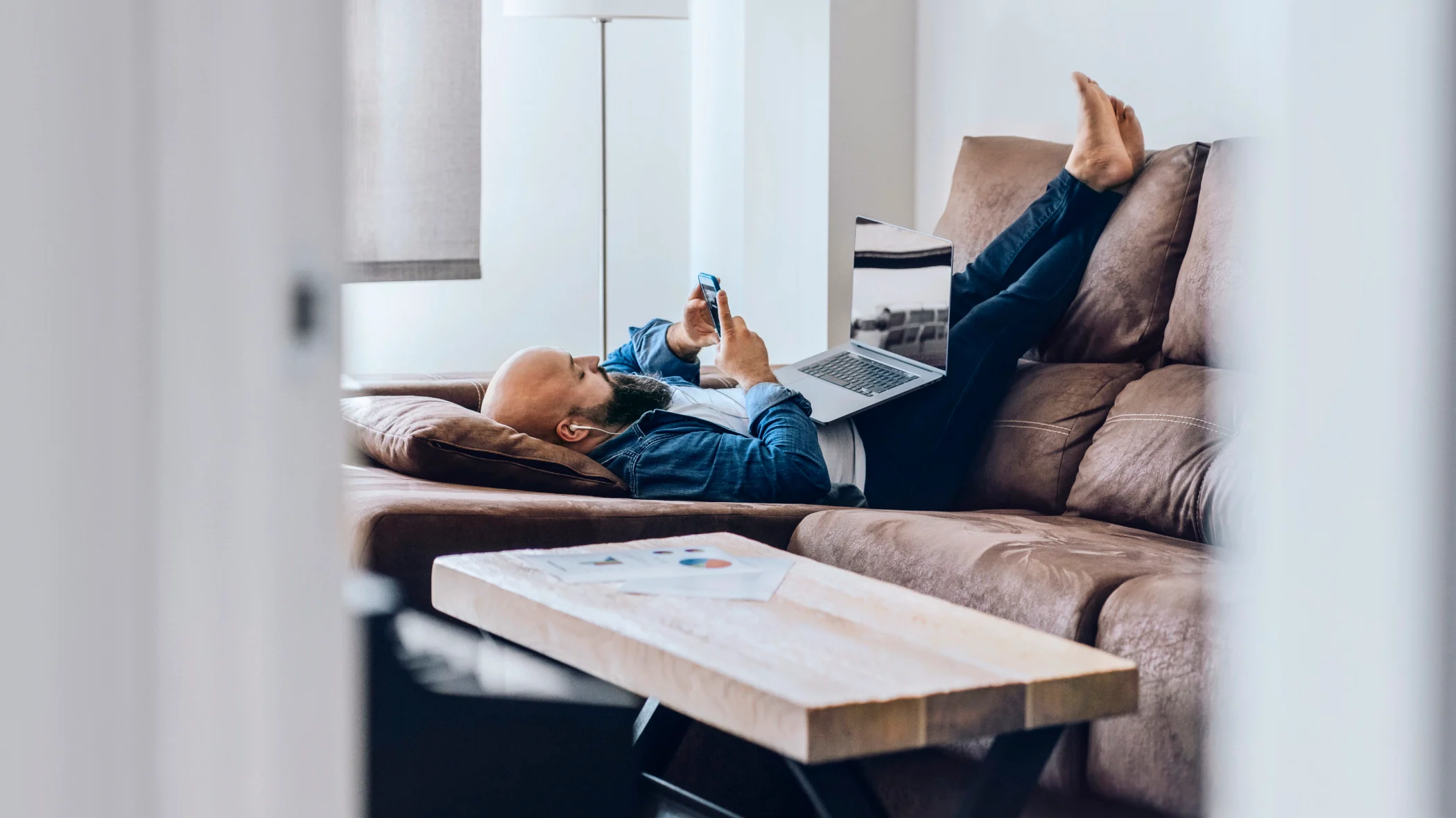 Ein Mann liegt auf dem Rücken auf der Couch und hat ein Handy in der Hand.