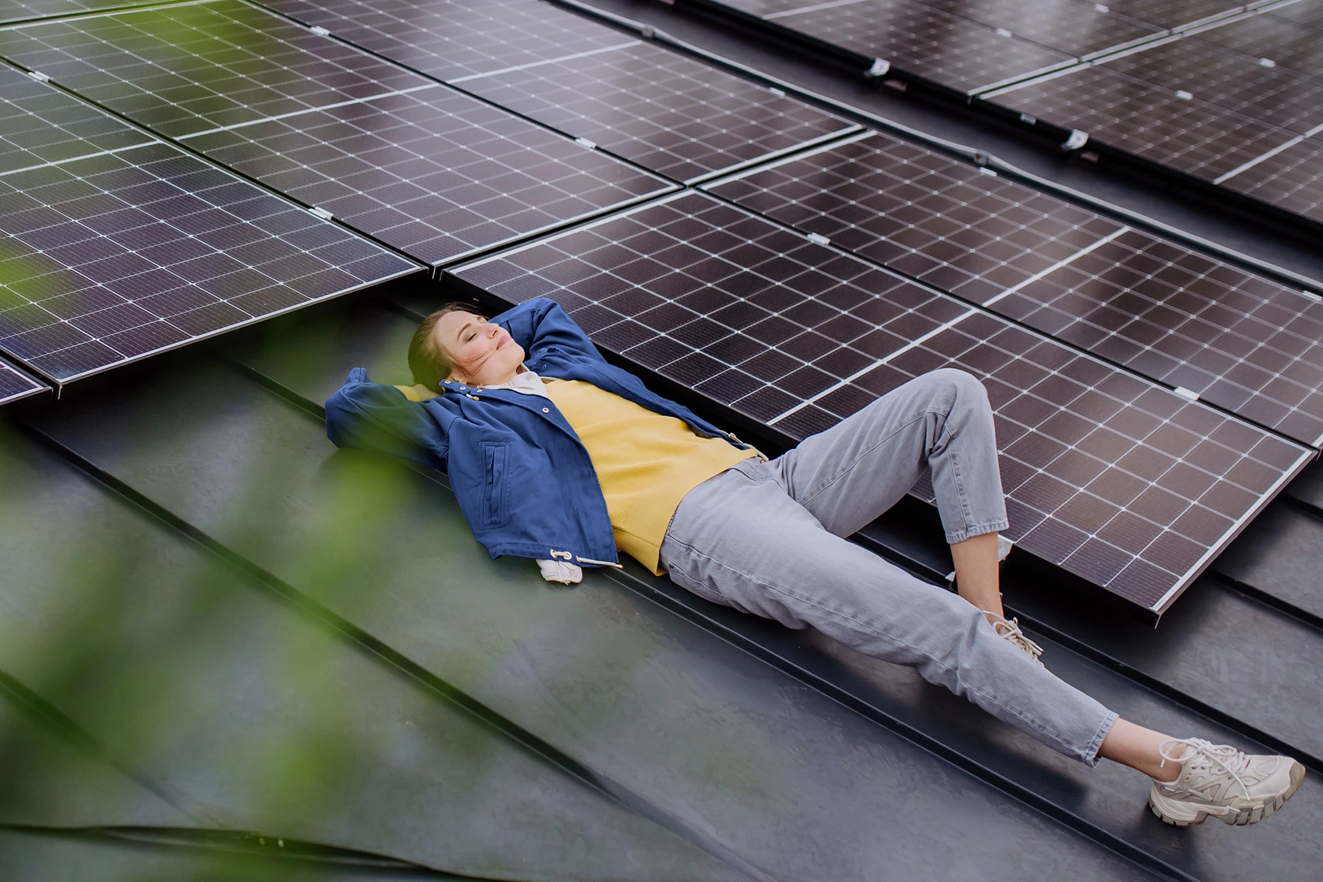 Frau liegt entspannt auf Hausdach neben Solarpanelen