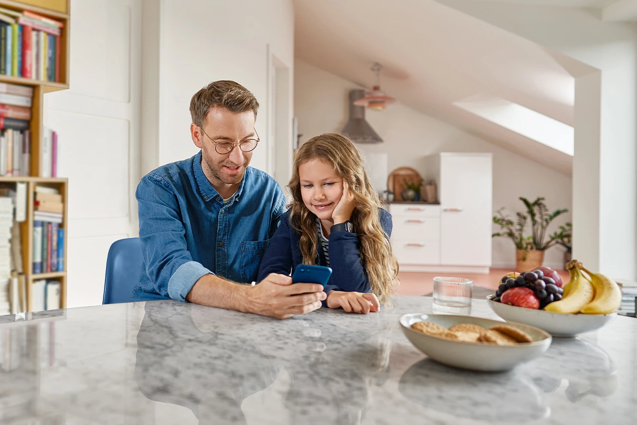 Mann und Kind sitzen mit Handy am Tisch