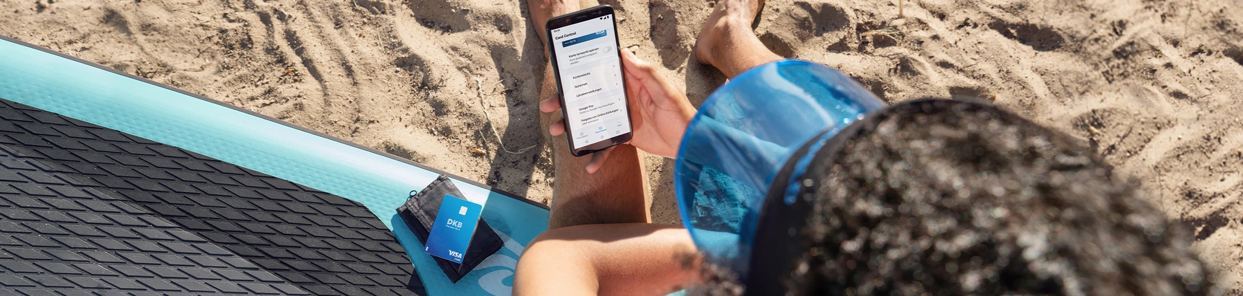 Person mit Smartphone und DKB Visa Card am Strand