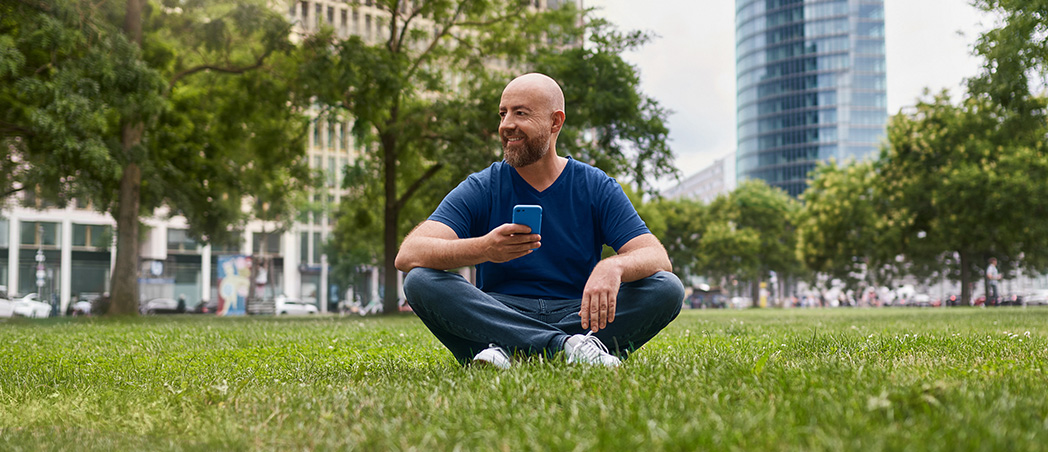 Mann mit Handy sitzt auf Wiese