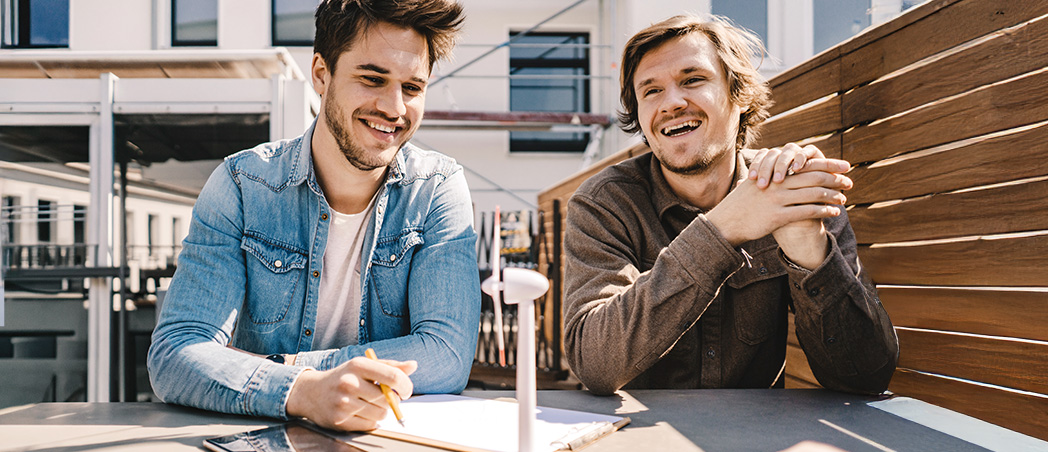 Zwei Männer sitzen an einem Tisch und lachen entspannt bei einem Gespräch