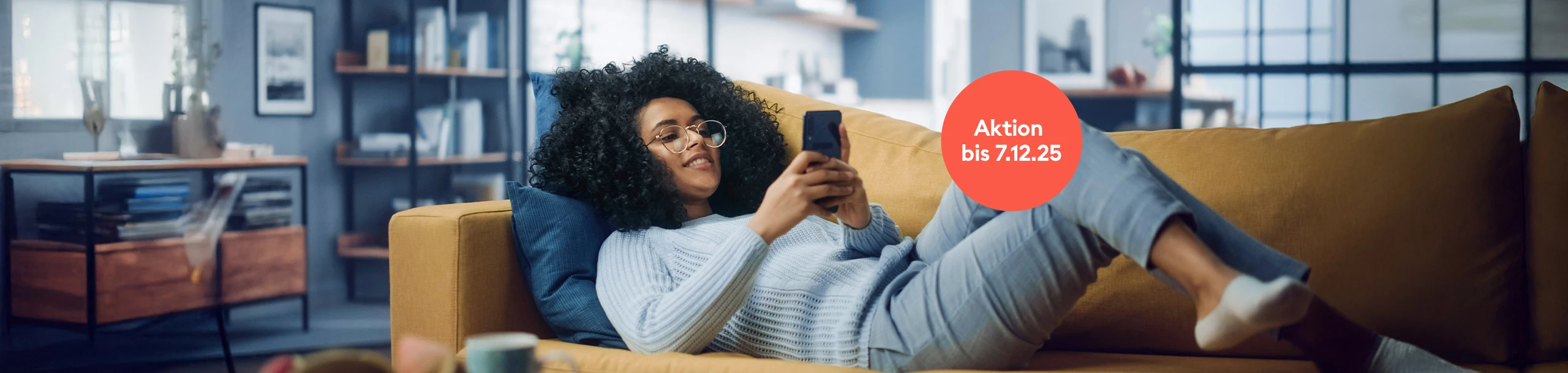 Junge Frau liegend auf Couch mit Handy in der Hand