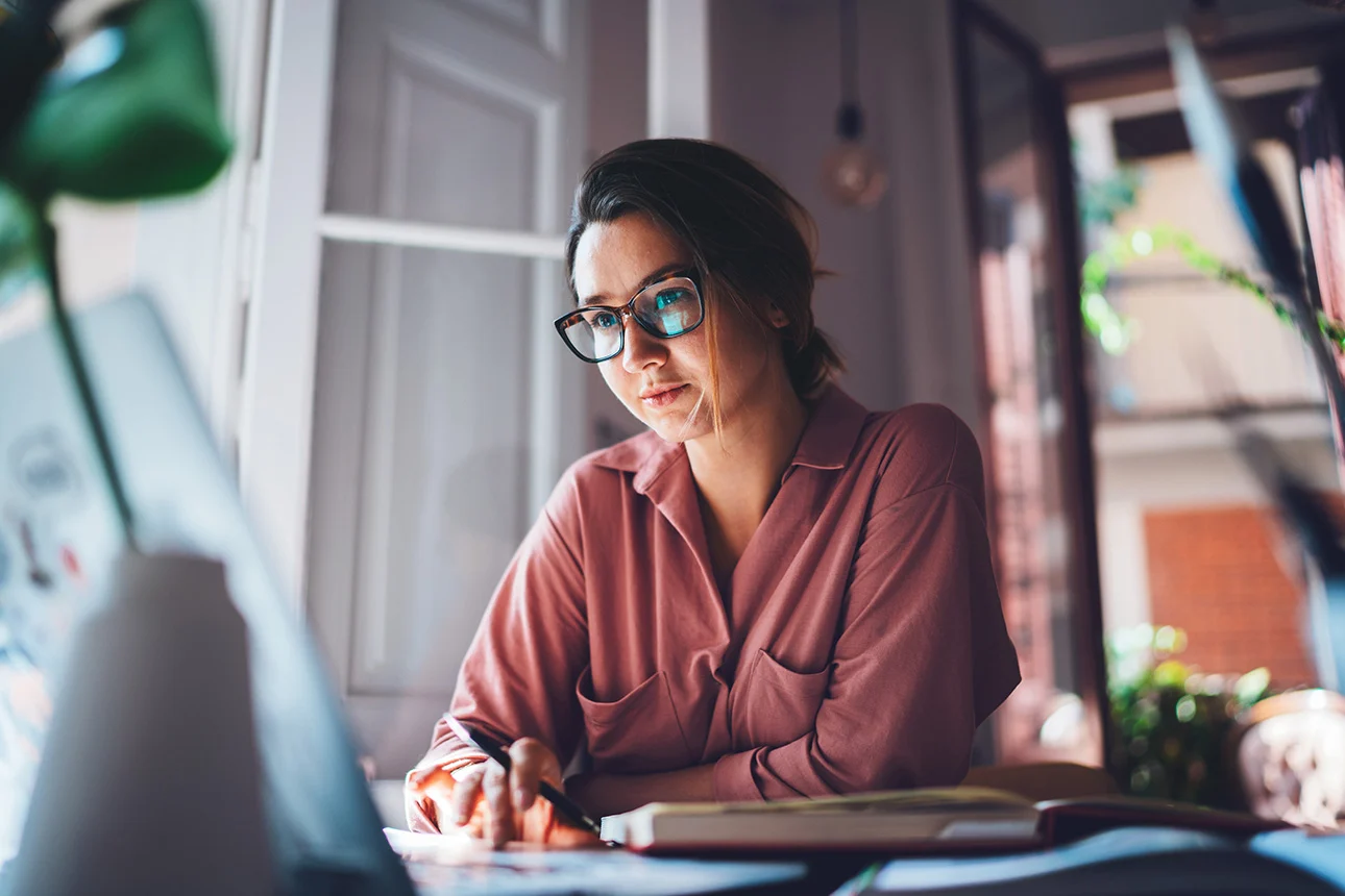 Eine Frau mit einem Stift in der Hand sitzt vor einem Laptop