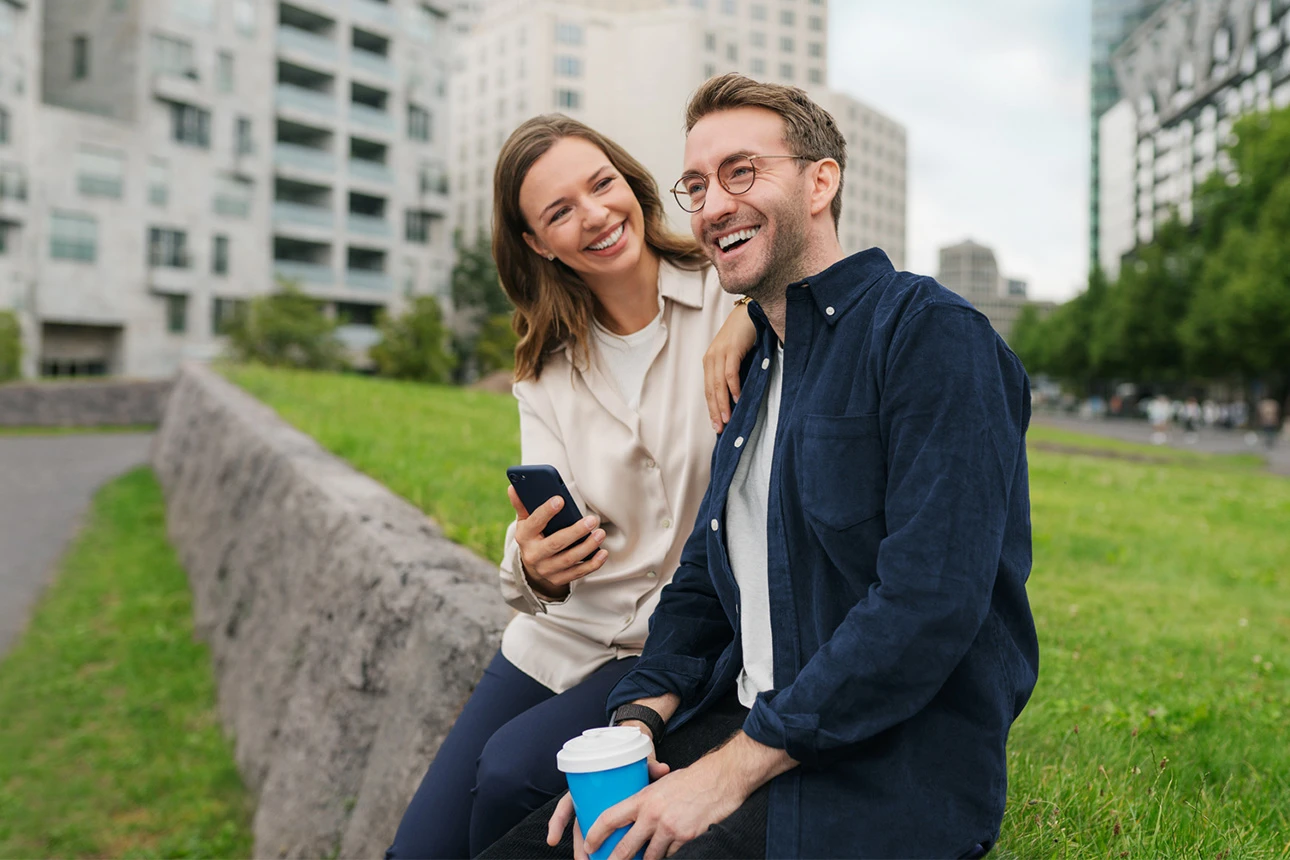 Paar sitzt auf Mauer mit Kaffeebecher und Handy