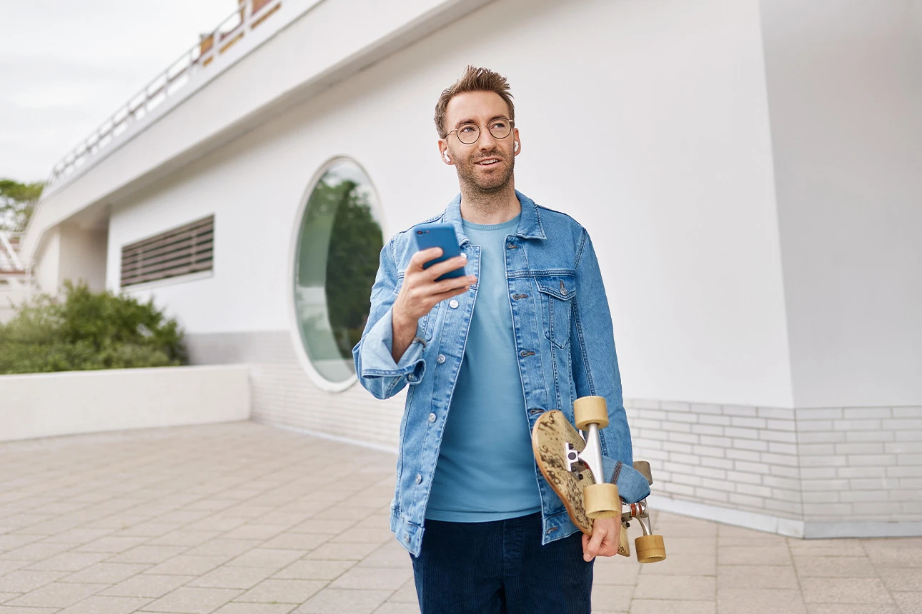 Ein Mann hält Skateboard und Smartphone in der Hand
