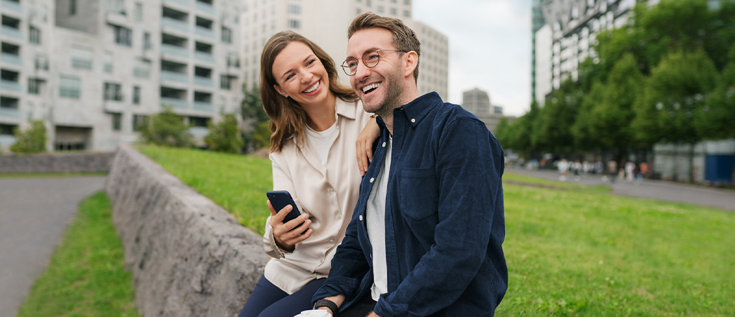 Paar sitzt auf Mauer mit Kaffeebecher und Handy