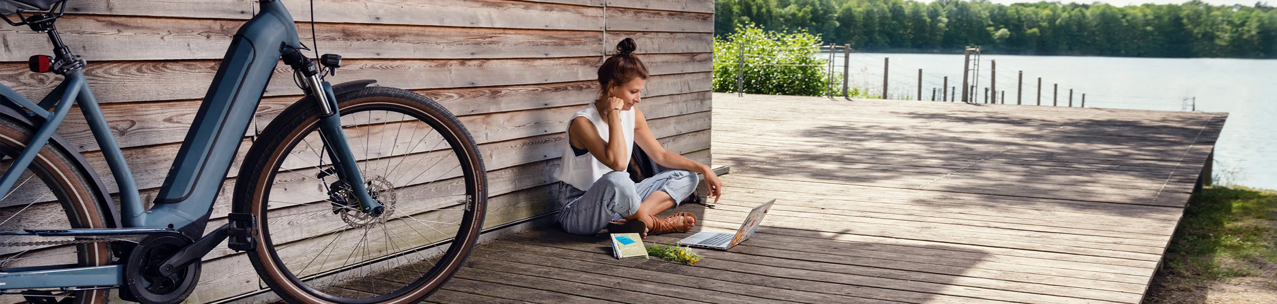 Frau sitzt am See mit Laptop und E-Bike