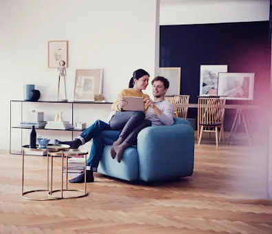 Ein junges Paar sitz gemeinsam mit Laptop auf einem Sofa im Wohnzimmer.