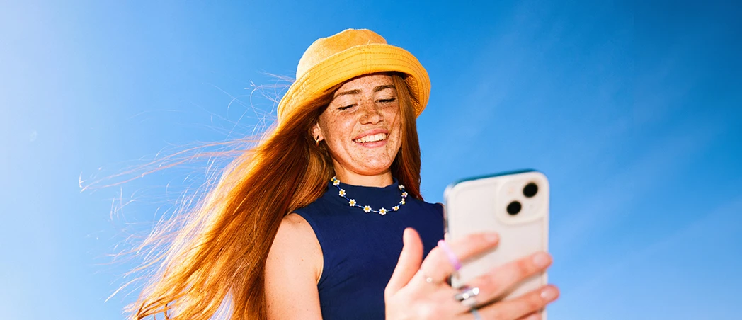 Lächelnde Frau mit Smartphone unter blauem Himmel
