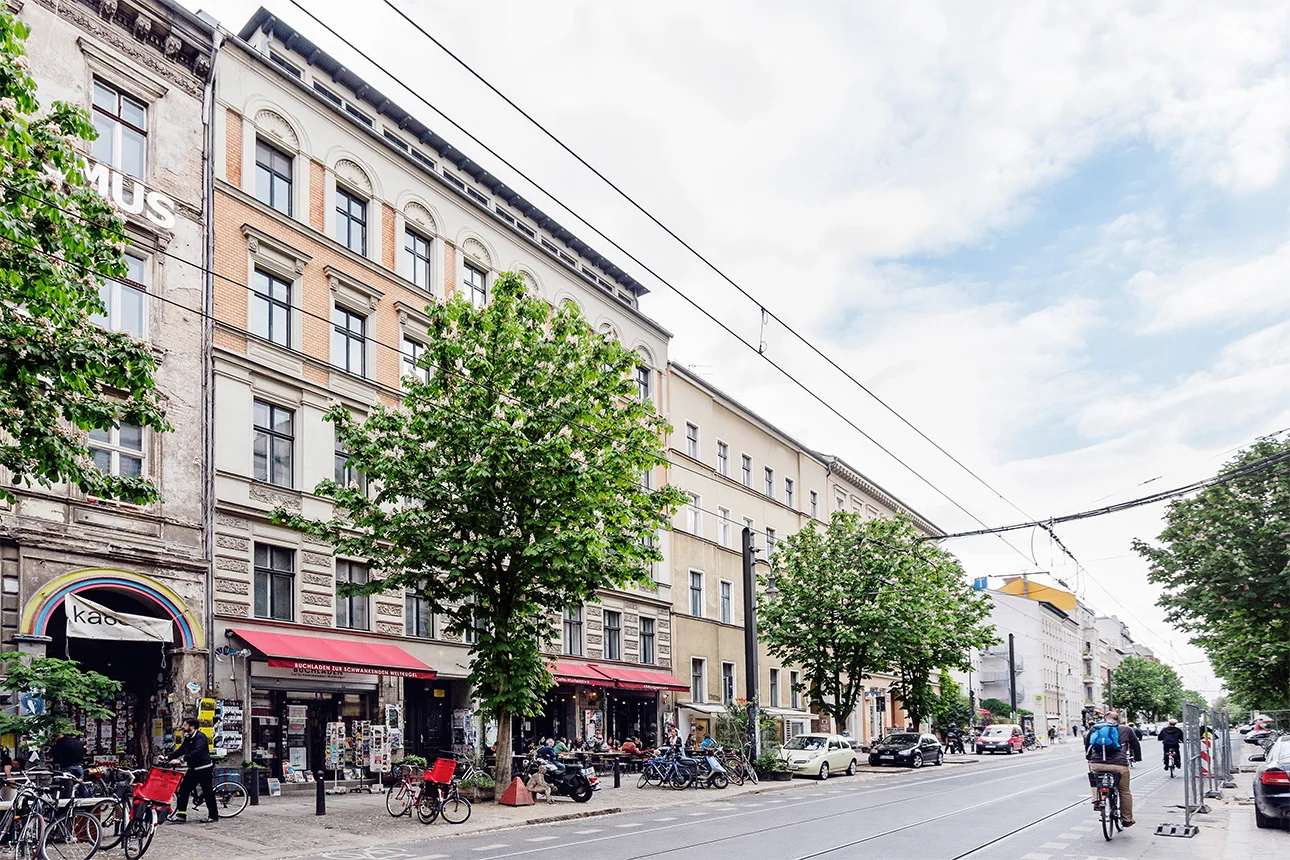 Schräger Blick auf die Fassade eines Altbau-Mehrfamilienhauses mit Geschäften im Erdgeschoss